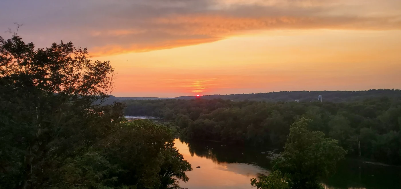 Summer foliage beneath a warm evening sky reflected in the Potomac.