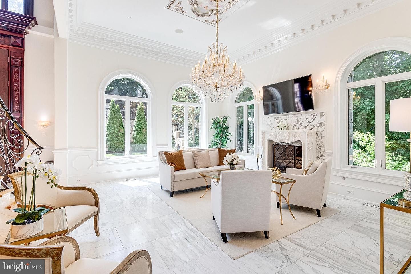 Formal living room with chandelier, carved marble fireplace and seating beside the grand staircase.